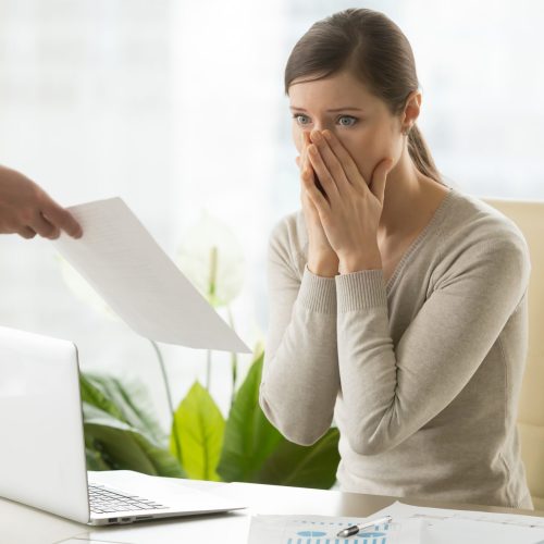 Young woman shocked when receiving dismissal notification from boss. Upset female employee worrying because of mistakes in calculations. Office worker can not believe in breaking employment contract